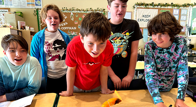 5 boys looking in awe at a small fire in a science experiment